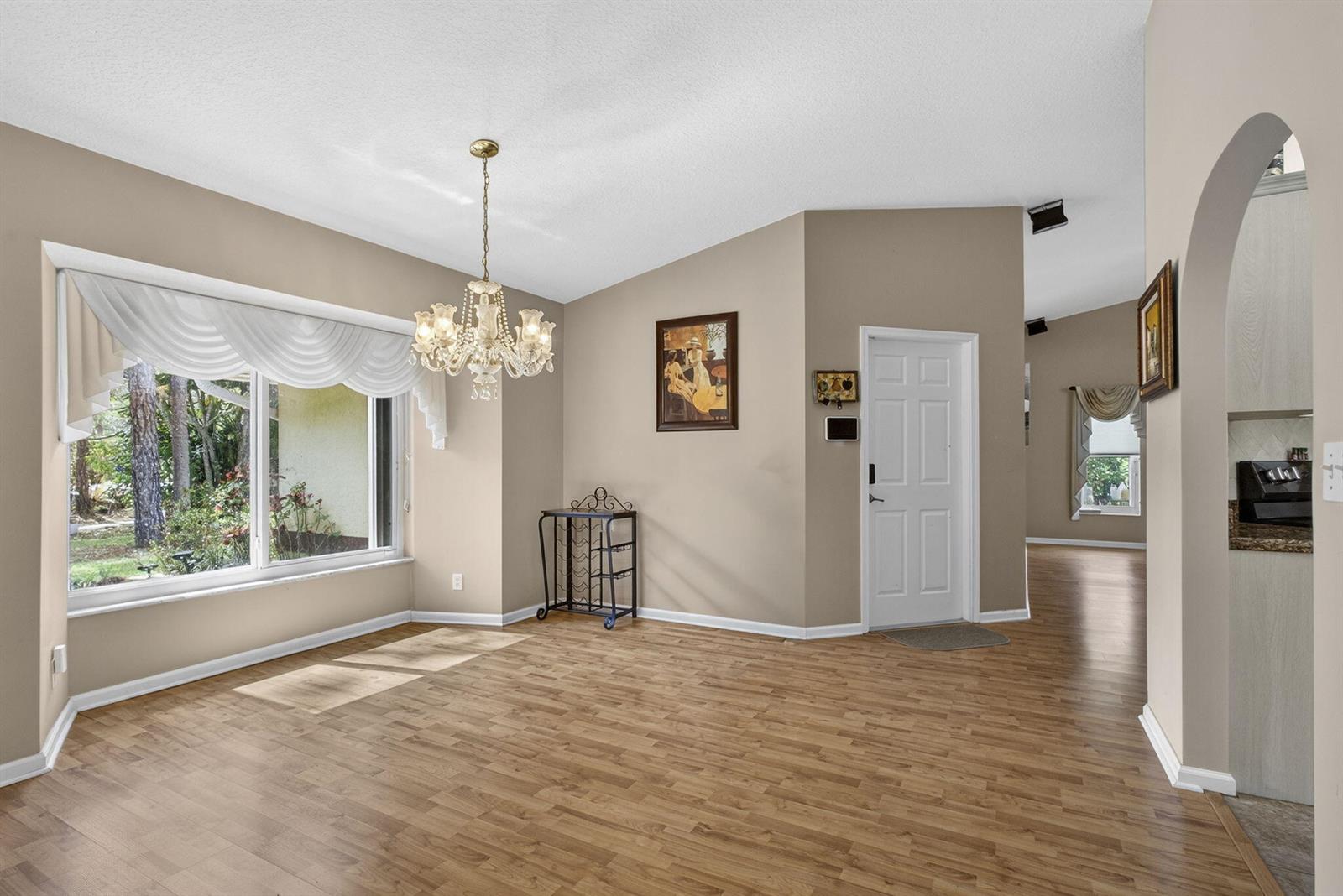 A dining room with wood-look flooring, a crystal chandelier, and a large window — 12751 Orange Boulevard, West Palm Beach FL 33412, WEST PALM BEACH, FL