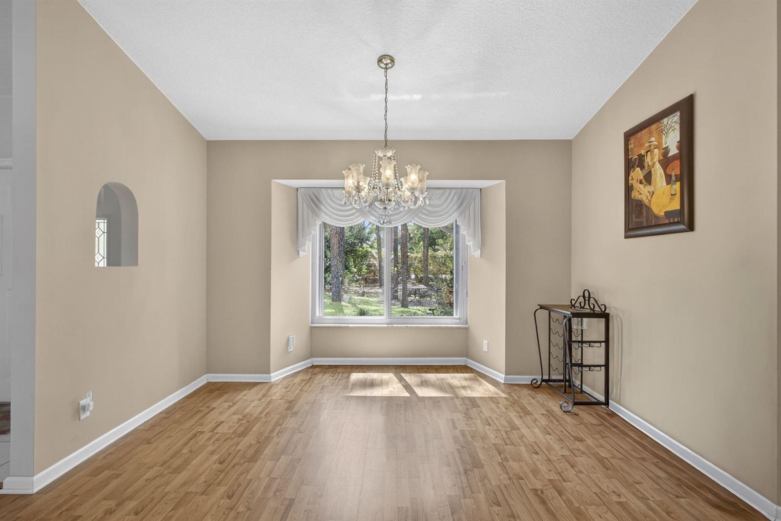 A dining room features light wood flooring, beige walls, a crystal chandelier, and a bay window — 12751 Orange Boulevard, West Palm Beach FL 33412, WEST PALM BEACH, FL