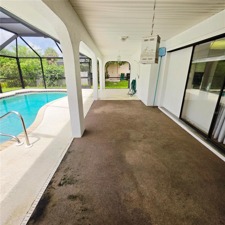 A covered patio with brown outdoor carpeting overlooks a swimming pool enclosed by a screen — 18563 FORT SMITH CIRCLE, PORT CHARLOTTE, FL