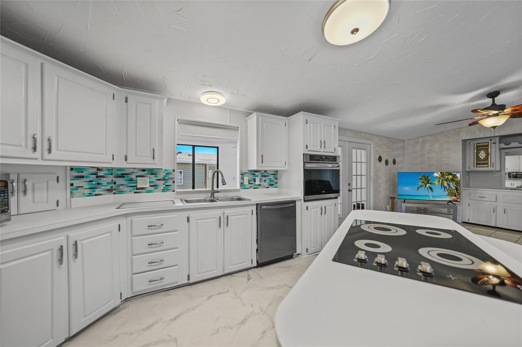 A white kitchen features a center island with a cooktop, tile backsplash, and stainless appliances — 495 SCHOONER STREET, NORTH PORT, FL