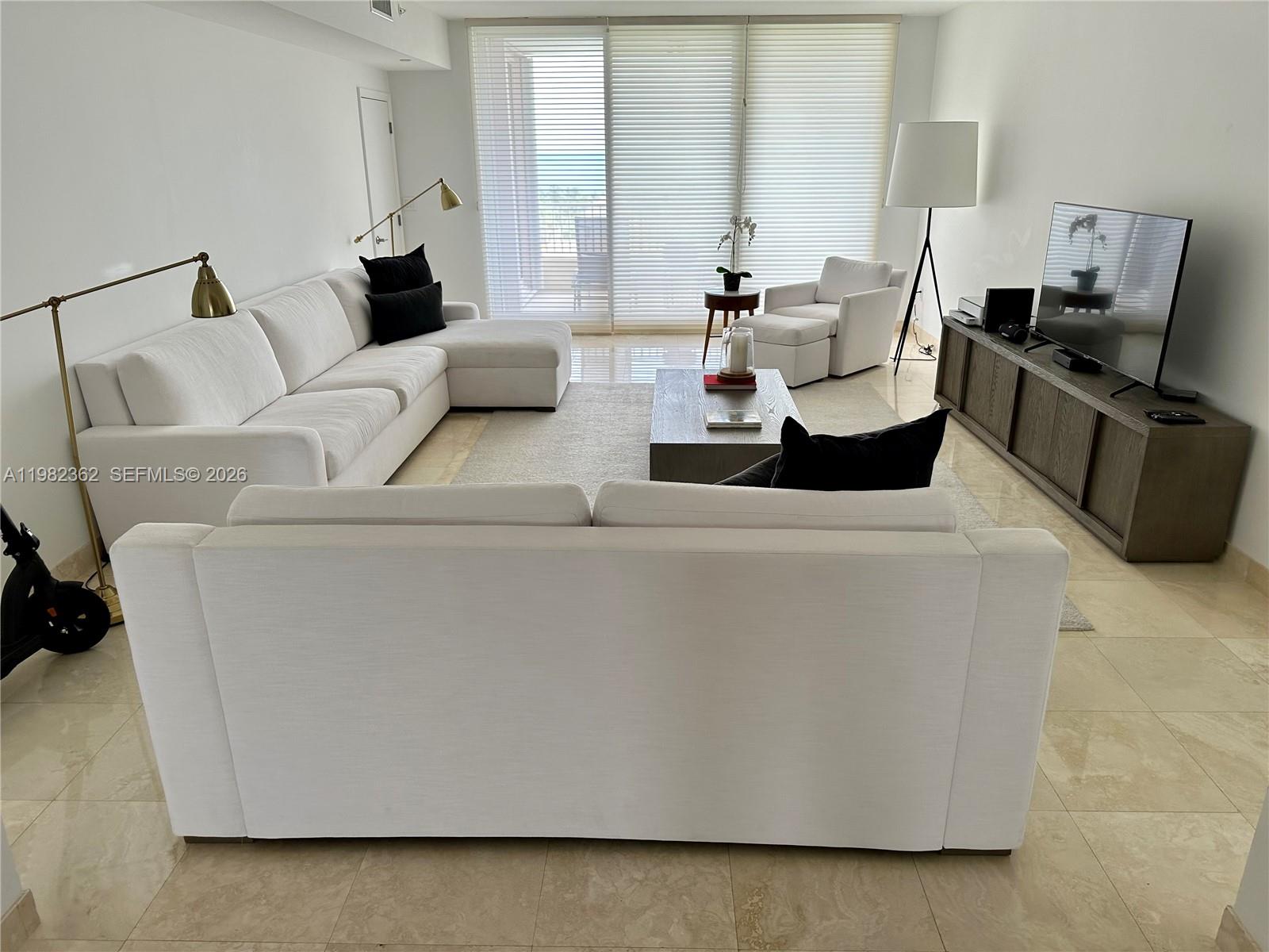 A bright living room features white sofas, a wooden coffee table, and a television console — 785 Crandon Blvd # 803, Key Biscayne FL 33149, KEY BISCAYNE, FL