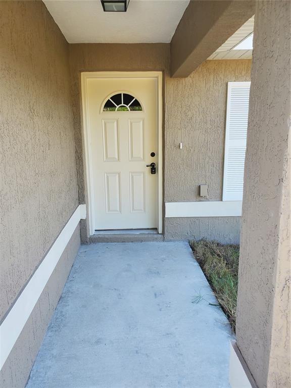 A beige front door with a small window sits under a covered entryway with stucco walls — 528 MARION OAKS LANE, OCALA, FL