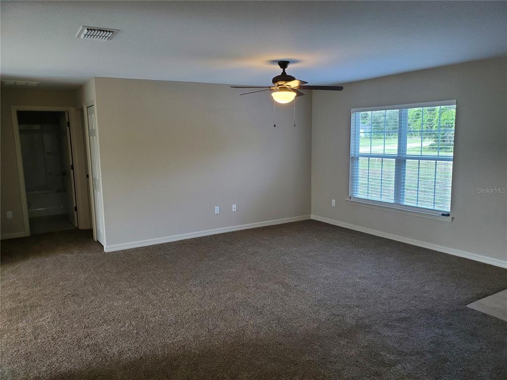 An empty bedroom features beige walls, brown carpeting, a ceiling fan, and a window — 528 MARION OAKS LANE, OCALA, FL