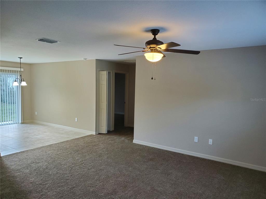 A living room with beige carpet, neutral walls, a ceiling fan, and an adjacent tiled area — 528 MARION OAKS LANE, OCALA, FL
