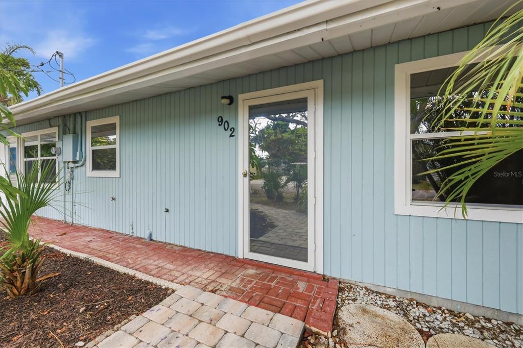 A light blue house exterior features a glass front door with the number 902 above — 902 37TH STREET W, BRADENTON, FL