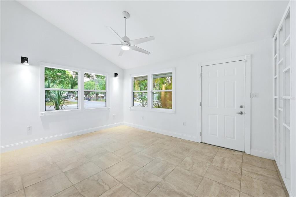 A bright, empty room features white walls, tile flooring, a ceiling fan, and large windows — 902 37TH STREET W, BRADENTON, FL