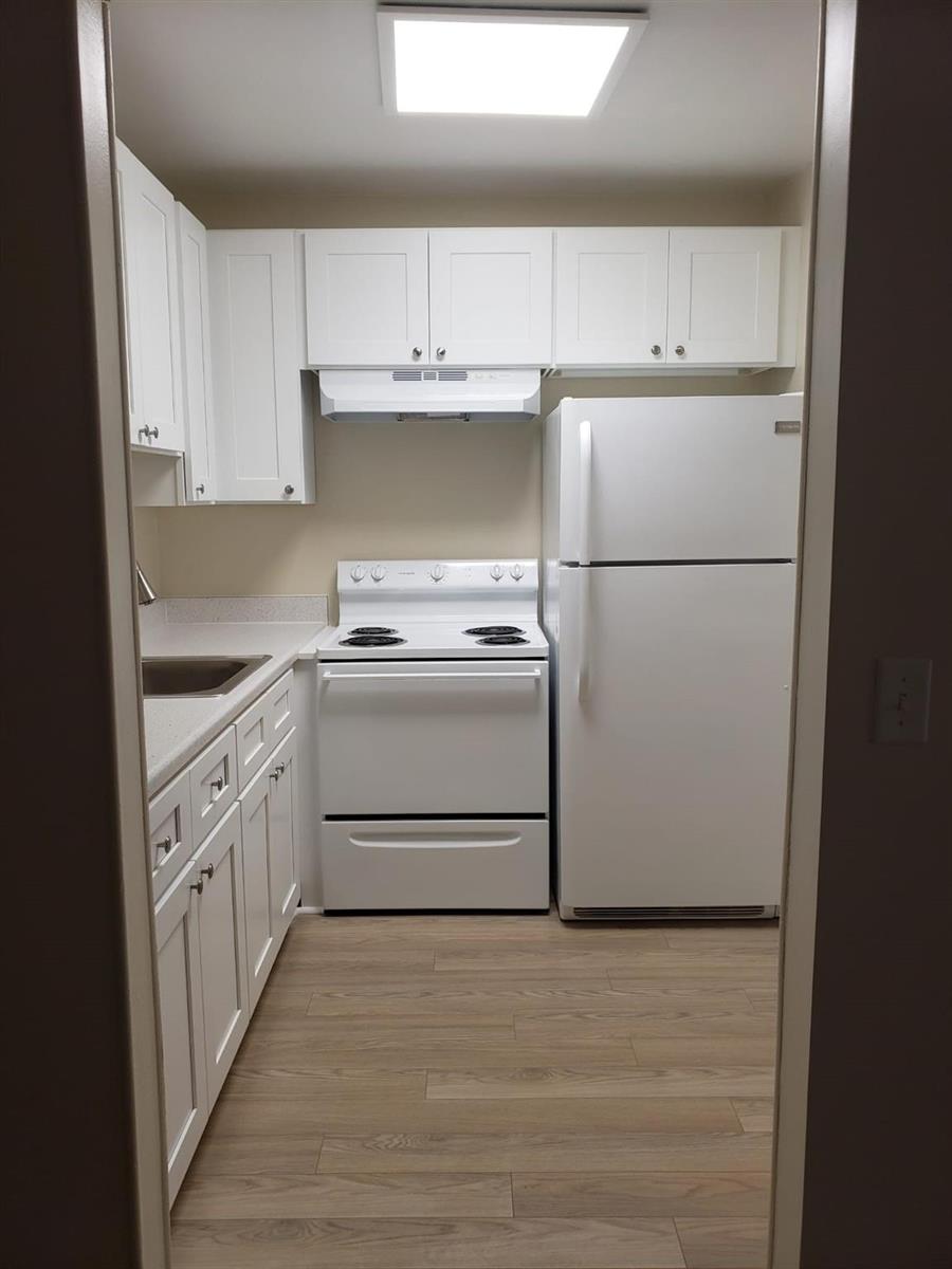 A galley kitchen features white cabinets, white appliances, light countertops, and wood-look flooring — 146 Canterbury # 146, West Palm Beach FL 33417, WEST PALM BEACH, FL