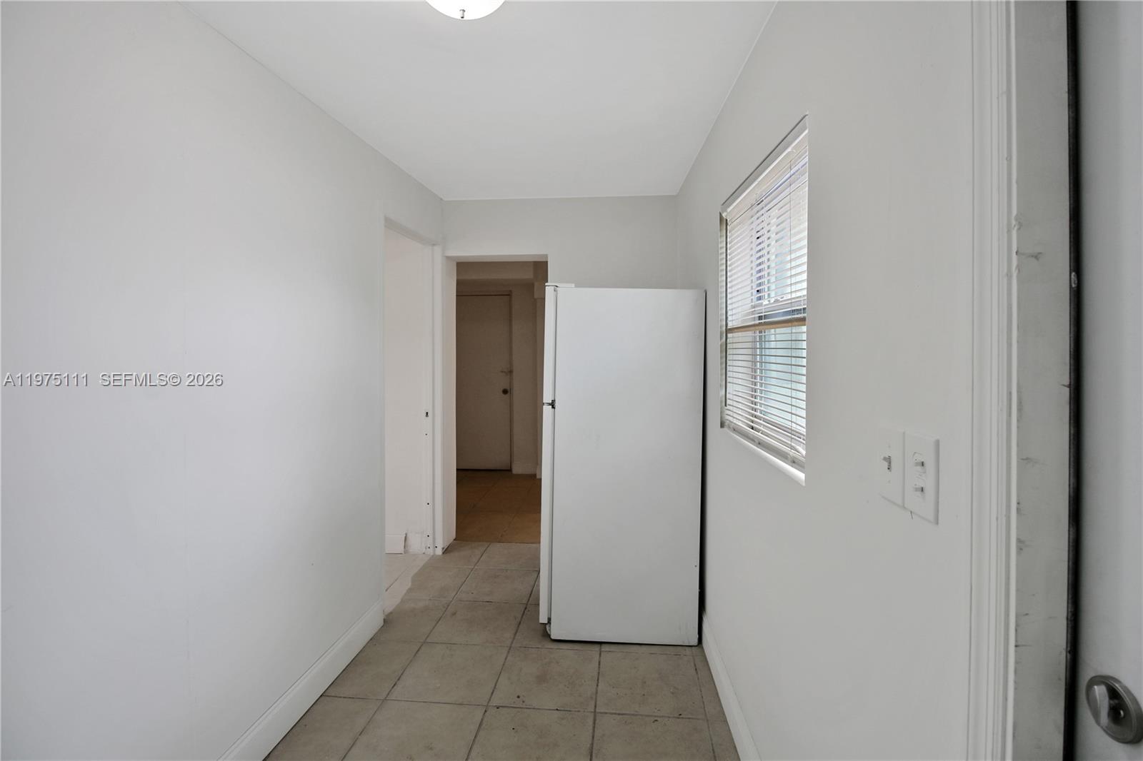 A narrow room with white walls, tile flooring, a window with blinds, and a white refrigerator — 1160 W 26 th  ct, Riviera Beach FL 33404, RIVIERA BEACH, FL