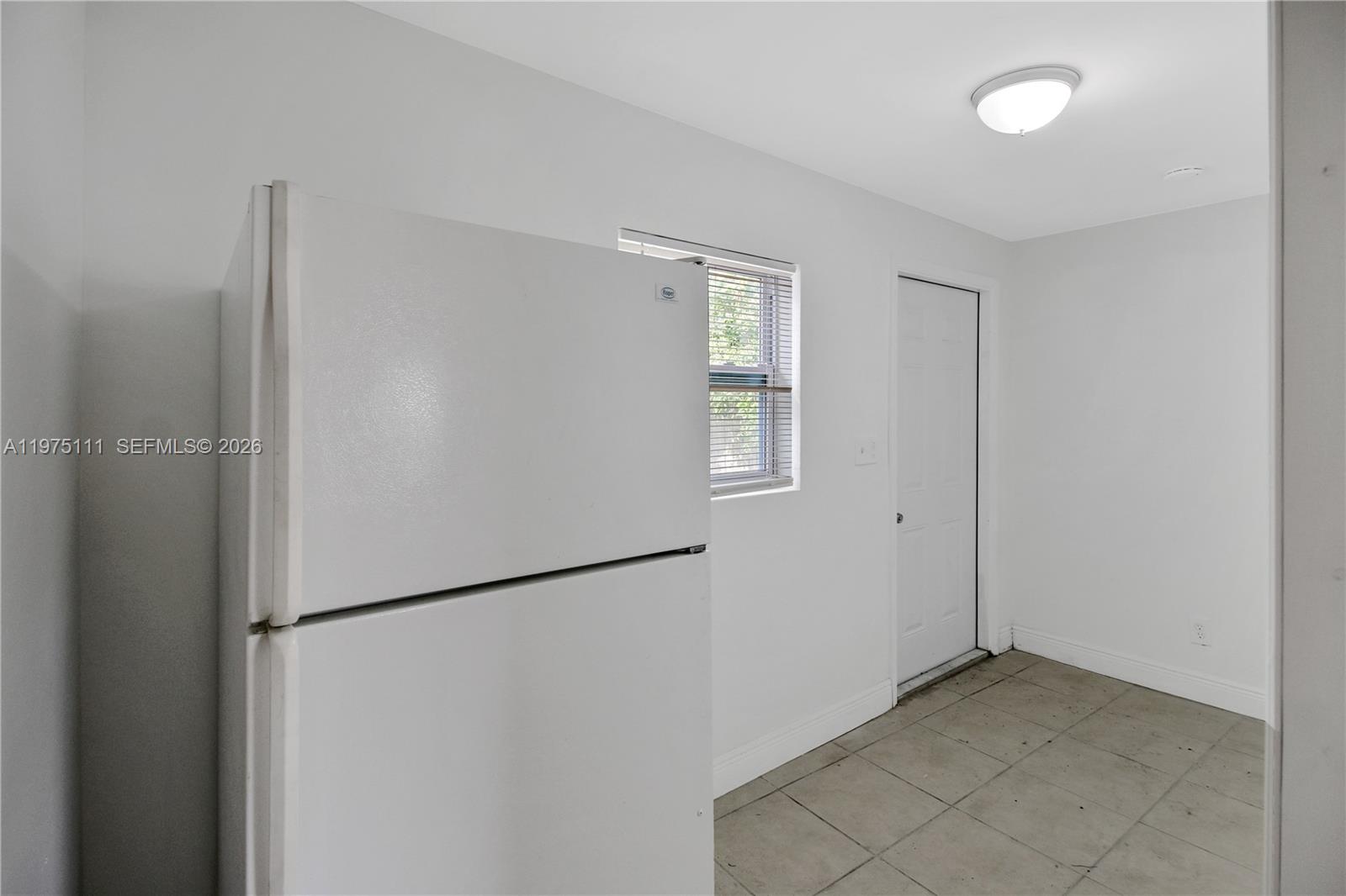 A white refrigerator stands in a room with white walls, tile floors, and a door — 1160 W 26 th  ct, Riviera Beach FL 33404, RIVIERA BEACH, FL