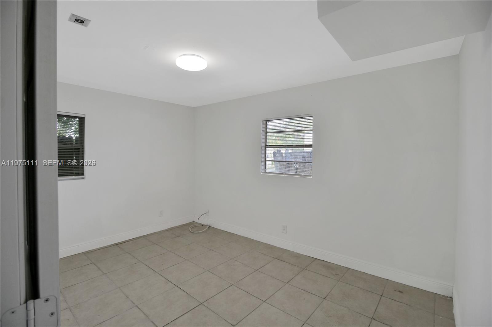 An empty room features white walls, light-colored tile flooring, two windows, and a ceiling light — 1160 W 26 th  ct, Riviera Beach FL 33404, RIVIERA BEACH, FL