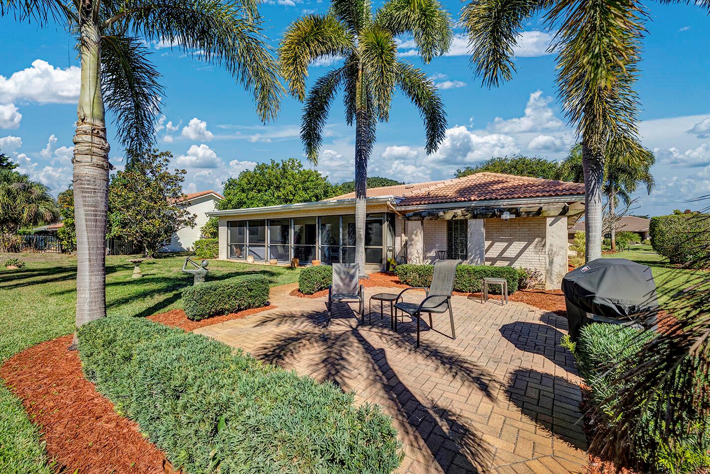 A backyard patio with a grill, outdoor seating, and palm trees behind a brick house — 5362 Piping Rock Drive, Boynton Beach FL 33437, BOYNTON BEACH, FL