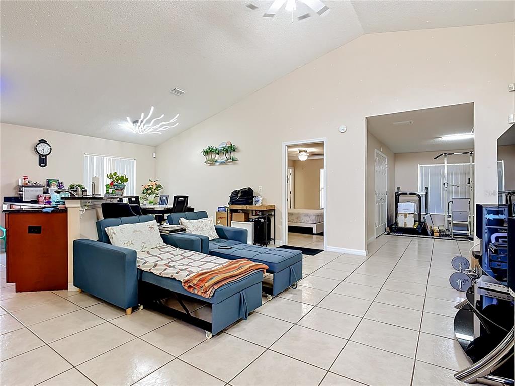 A living room with tiled floors, a blue sectional sofa, and an adjacent dining area — 1036 DUDLEY DRIVE, KISSIMMEE, FL