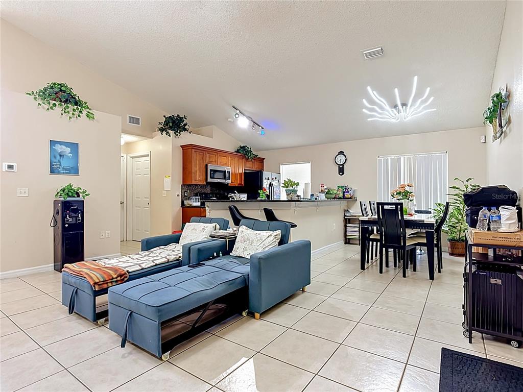 An open-concept living and dining area features tile flooring, blue furniture, and a kitchen island — 1036 DUDLEY DRIVE, KISSIMMEE, FL