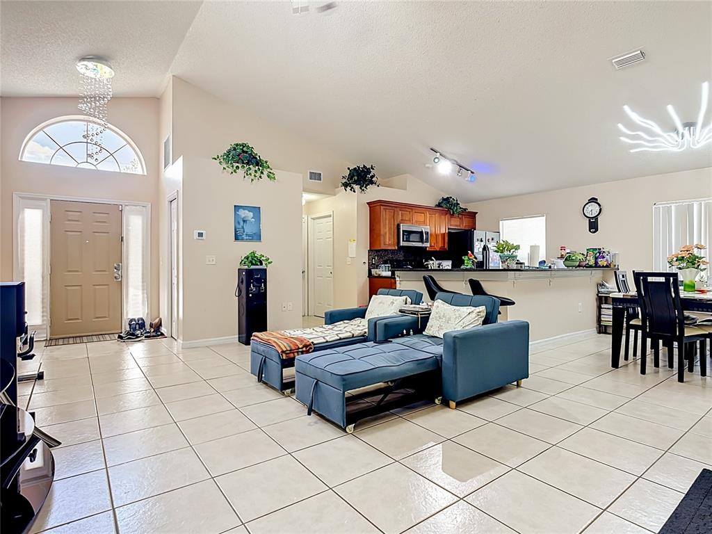 An open-concept living and dining area features tile flooring, vaulted ceilings, and a kitchen island — 1036 DUDLEY DRIVE, KISSIMMEE, FL