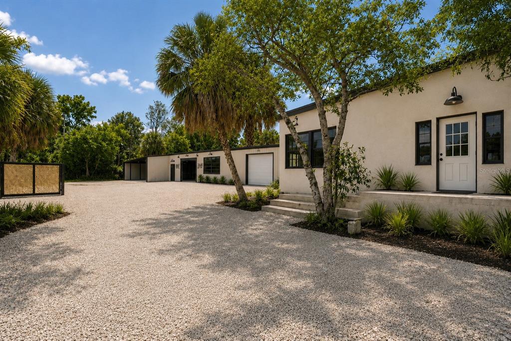 A gravel driveway leads to a white building with a white door and adjacent garage bays — 4214 W VIRGINIA AVE UNIT 7, TAMPA, FL