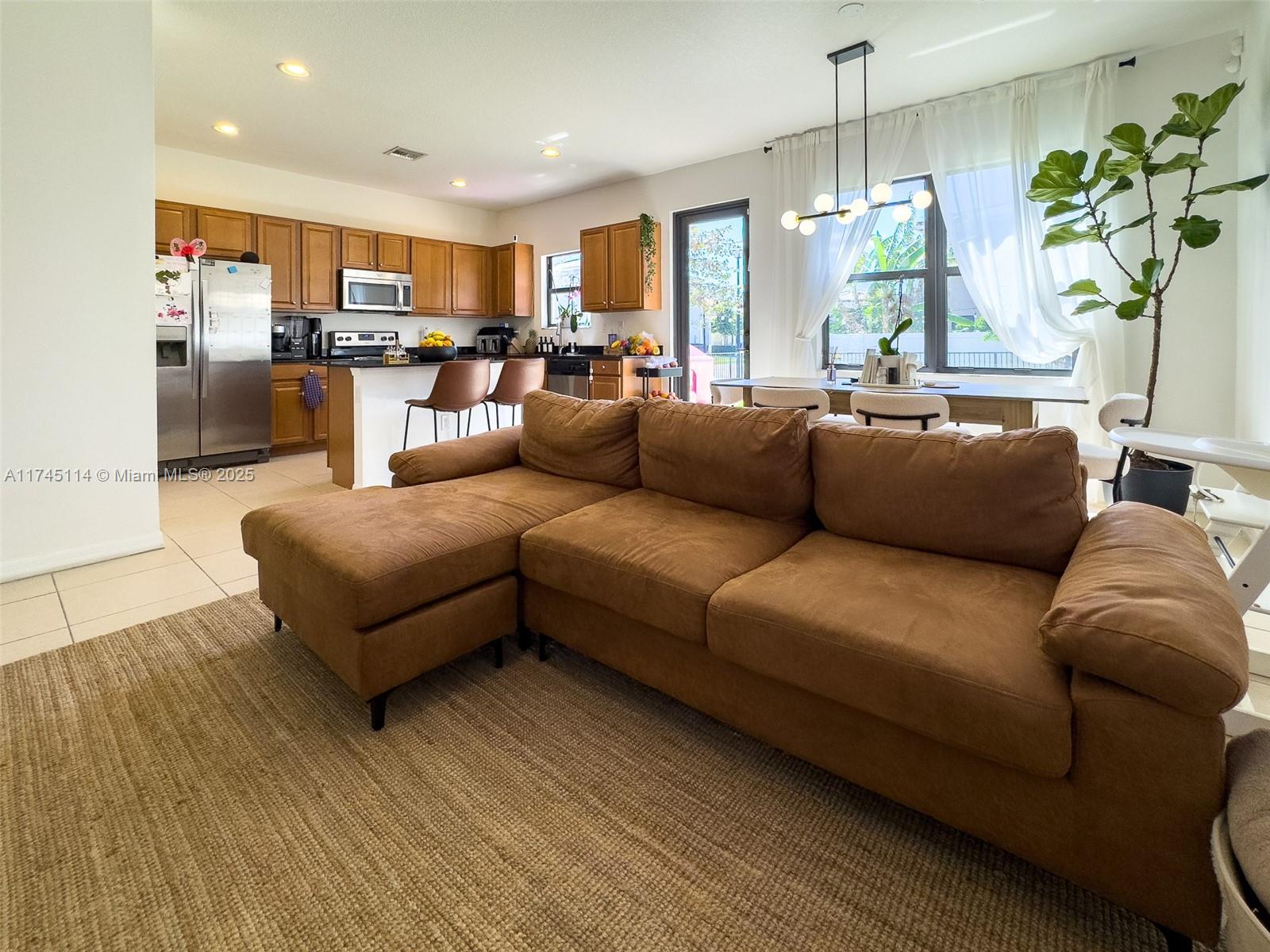 A brown sectional sofa sits on a rug in an open-concept living and dining area — 686 NE 191st Ter, Miami FL 33179, MIAMI, FL
