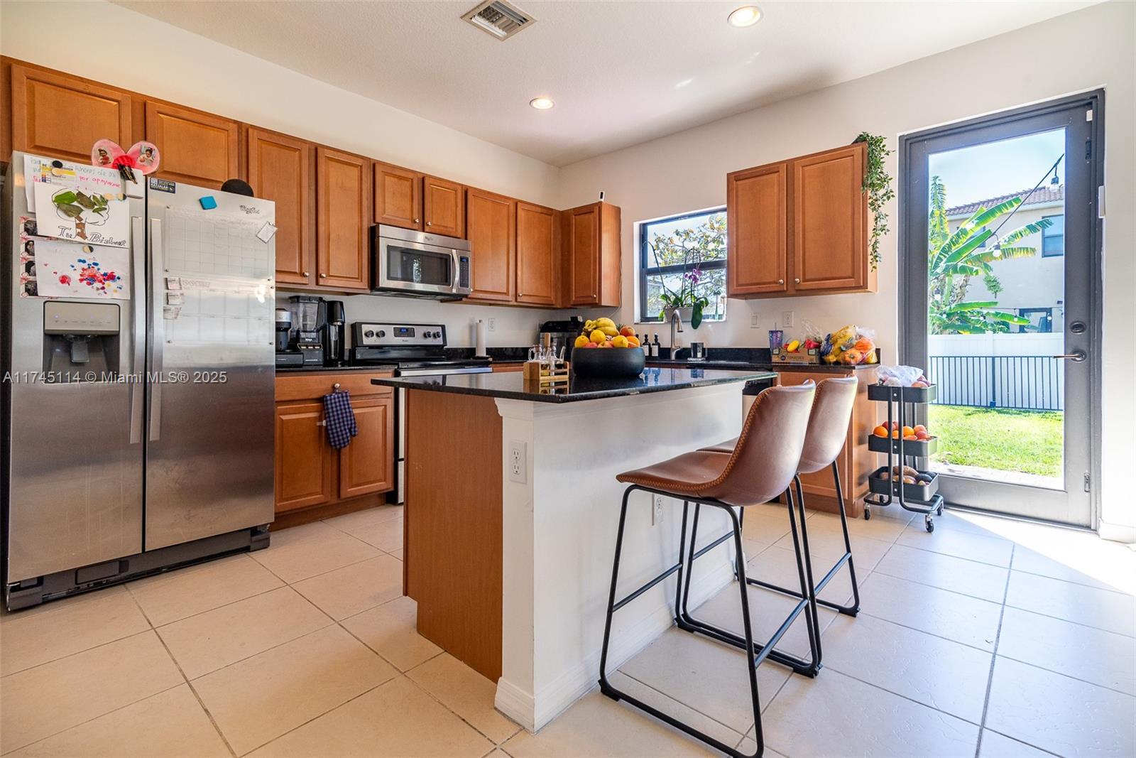 A kitchen features wood cabinets, black granite countertops, a central island, and a glass door — 686 NE 191st Ter, Miami FL 33179, MIAMI, FL