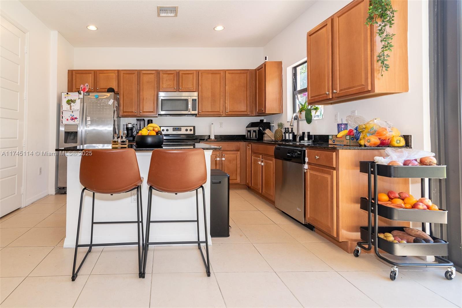 A kitchen features wood cabinets, stainless steel appliances, a center island with stools, and tile flooring — 686 NE 191st Ter, Miami FL 33179, MIAMI, FL