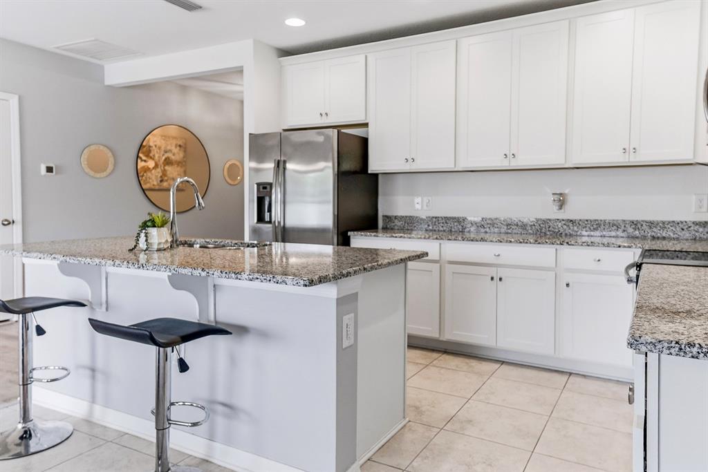 A kitchen features white cabinets, granite countertops, a center island with bar stools, and appliances — 12103 GOTHIC ROAD, SPRING HILL, FL