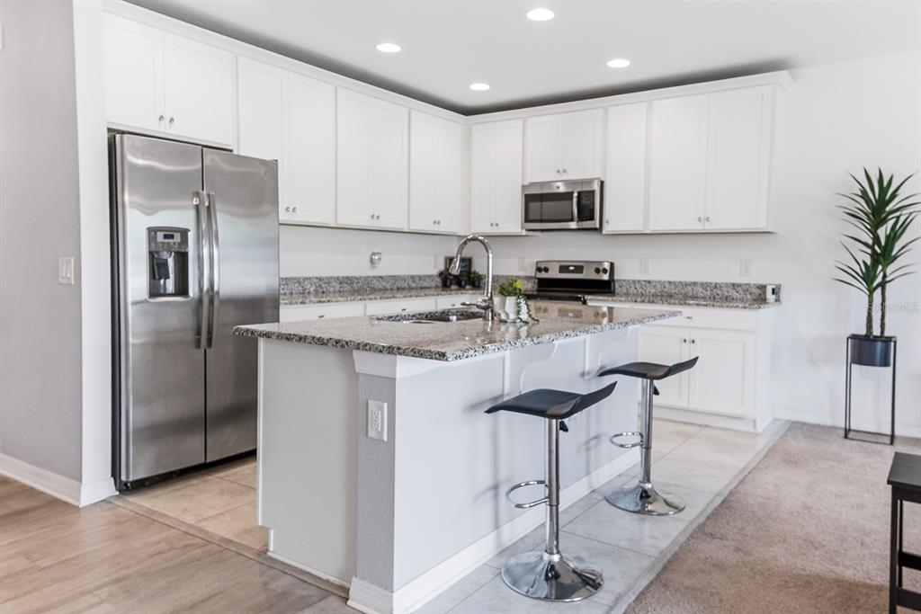 A modern kitchen features white cabinets, granite countertops, stainless steel appliances, and a breakfast island — 12103 GOTHIC ROAD, SPRING HILL, FL