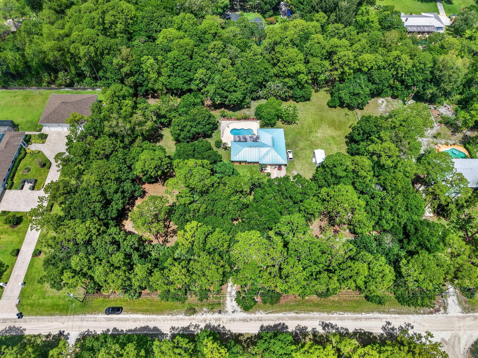 An aerial view shows a house with a blue roof and pool surrounded by dense trees — 15721 111th Terrace N, Jupiter FL 33478, JUPITER, FL