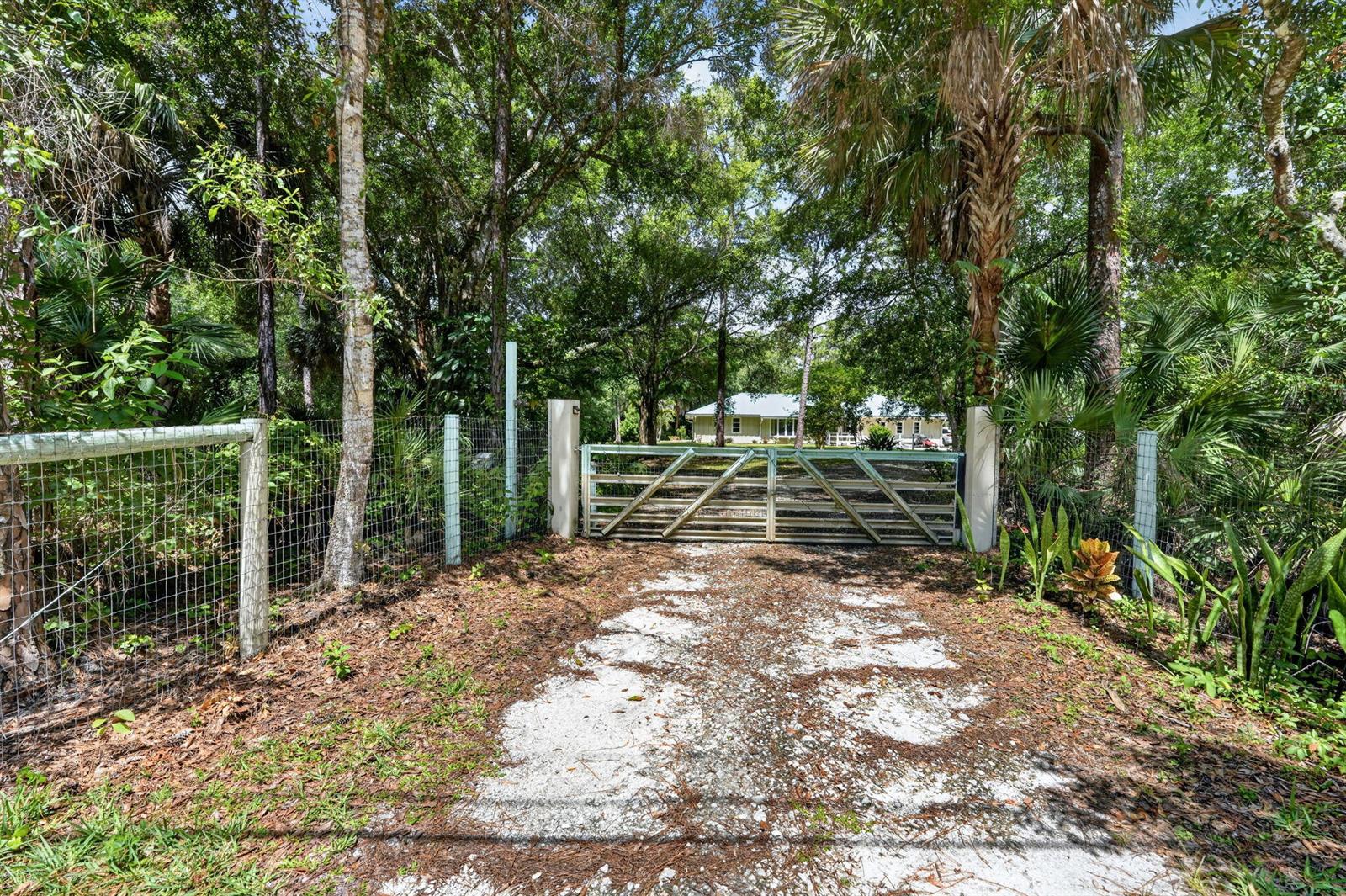 A gravel driveway leads to a closed metal gate in front of a wooded property — 15721 111th Terrace N, Jupiter FL 33478, JUPITER, FL