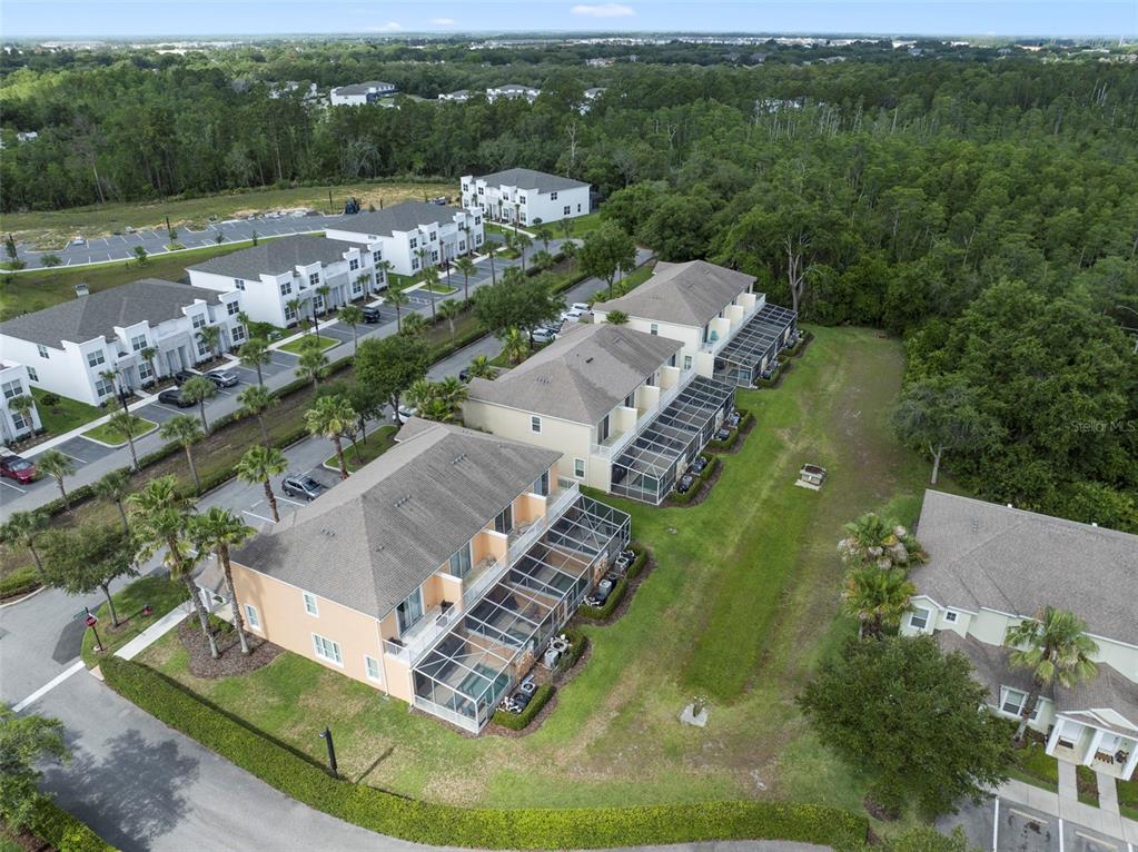 An aerial view shows multi-story townhomes with screened-in lanais and surrounding green space — 17349 SERENIDAD BOULEVARD, CLERMONT, FL