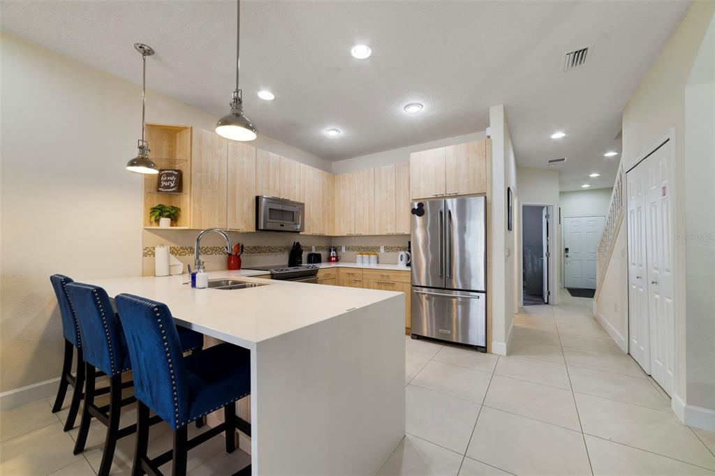 A kitchen features light wood cabinets, a white island with blue stools, and stainless appliances — 17349 SERENIDAD BOULEVARD, CLERMONT, FL