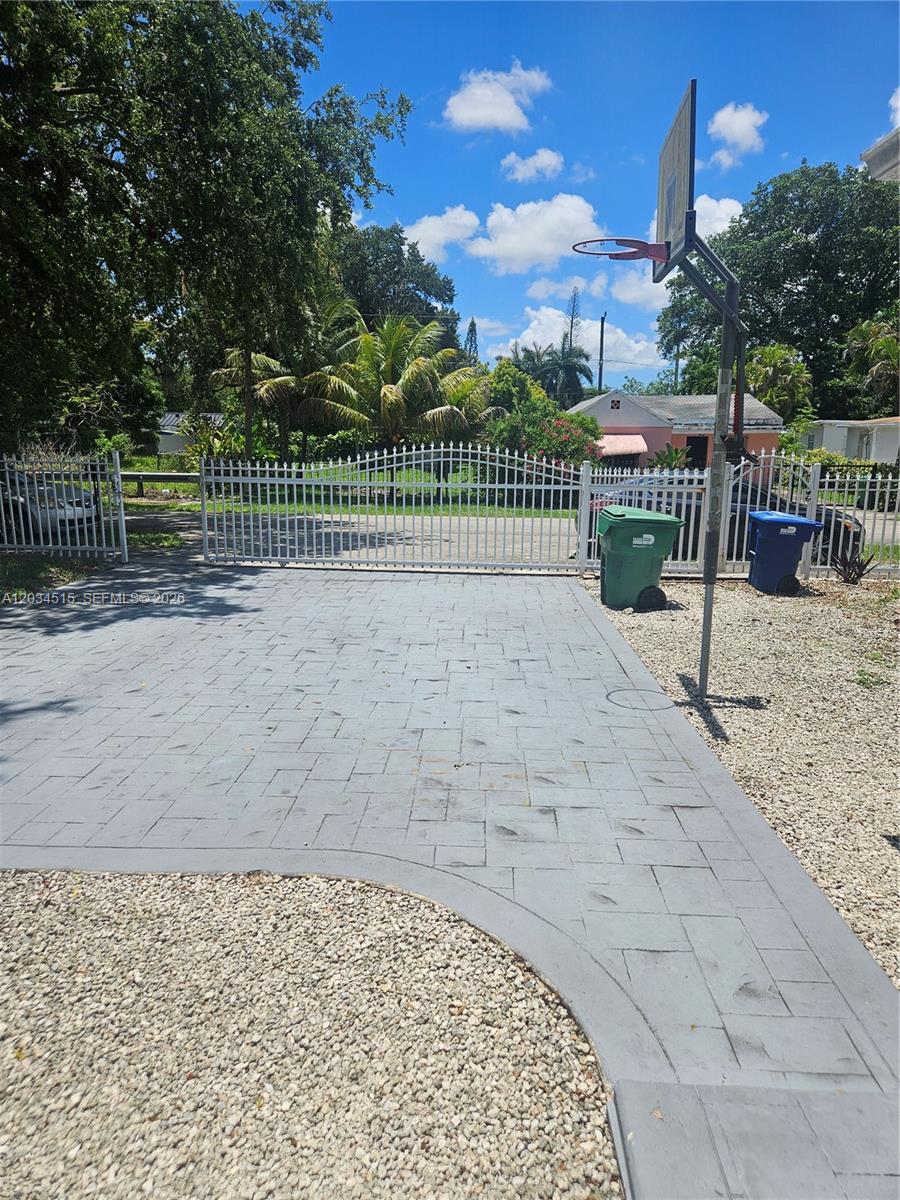 A paved driveway leads to a white metal gate with a basketball hoop nearby — 1905 NW 113th Ter, Miami FL 33167, MIAMI, FL