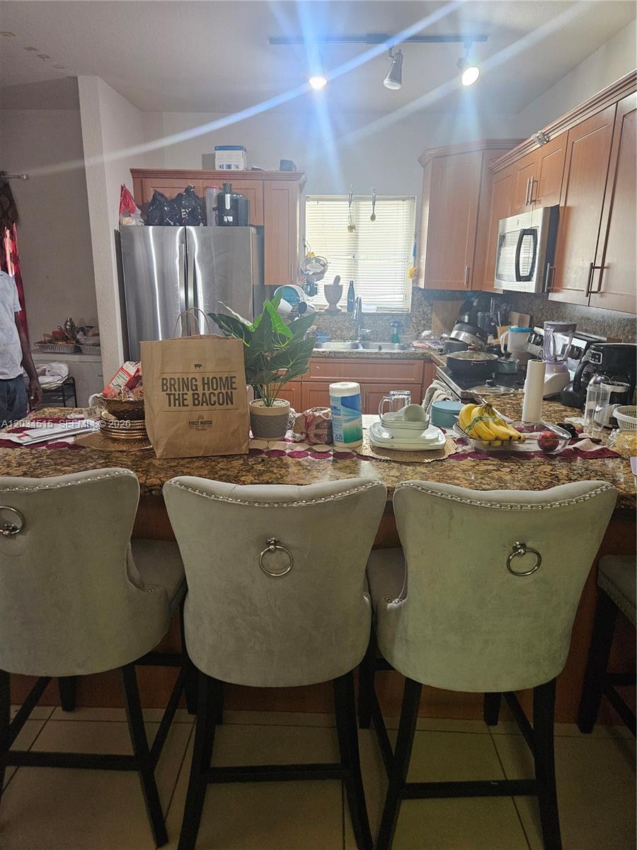 A kitchen features wood cabinets, granite countertops, a breakfast bar with three chairs, and appliances — 1905 NW 113th Ter, Miami FL 33167, MIAMI, FL
