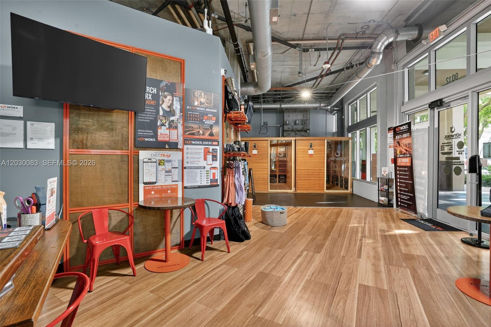A gym interior featuring wood-look flooring, red chairs, sauna units, and exposed industrial ceiling pipes — 9012 S Dadeland Blvd, Miami FL 33156, MIAMI, FL