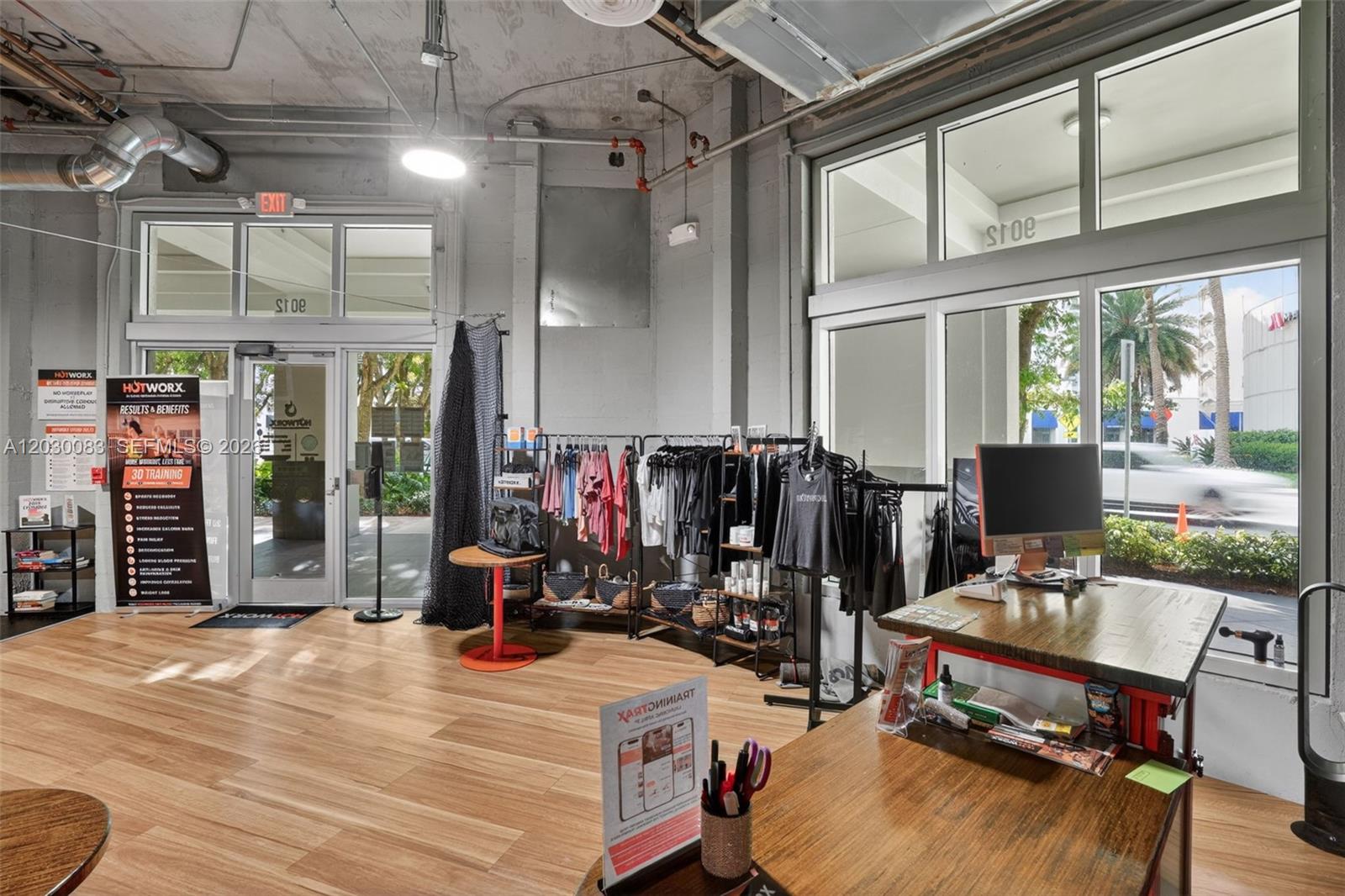 This commercial space features wood-look flooring, exposed industrial ceilings, and large windows with clothing racks — 9012 S Dadeland Blvd, Miami FL 33156, MIAMI, FL