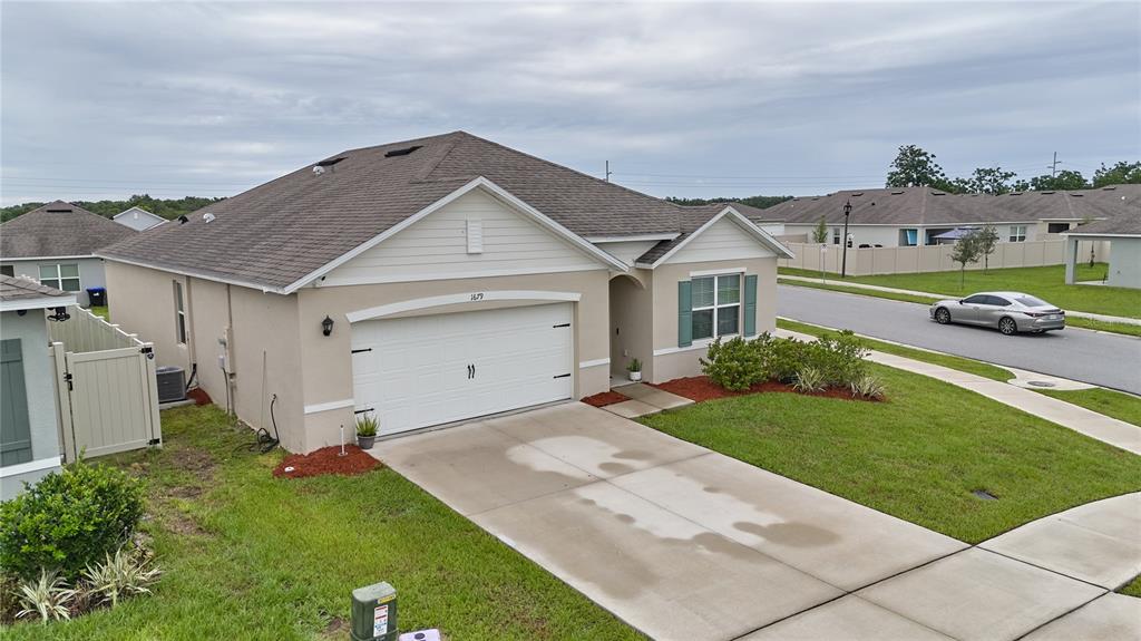A tan, single-story suburban house with a white garage door and a concrete driveway — 1679 AURORA RIDGE DRIVE, ZELLWOOD, FL