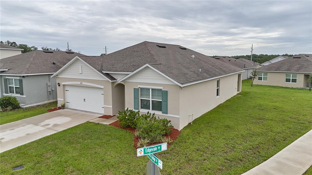 A single-story suburban house with a two-car garage and a street sign in front — 1679 AURORA RIDGE DRIVE, ZELLWOOD, FL