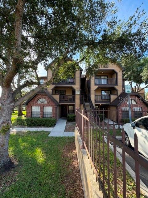A three-story apartment building with tan siding and a brown metal fence in the foreground — 355 LAKEPOINTE DRIVE UNIT 304, ALTAMONTE SPRINGS, FL