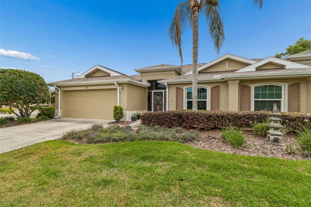A single-story house with a tan stucco exterior, a two-car garage, and a palm tree — 2006 GRANTHAM GREENS DRIVE UNIT 0, SUN CITY CENTER, FL