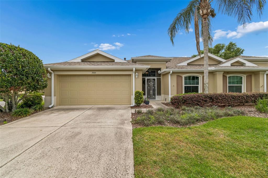 A tan single-story house with a two-car garage, a palm tree, and a front lawn — 2006 GRANTHAM GREENS DRIVE UNIT 0, SUN CITY CENTER, FL