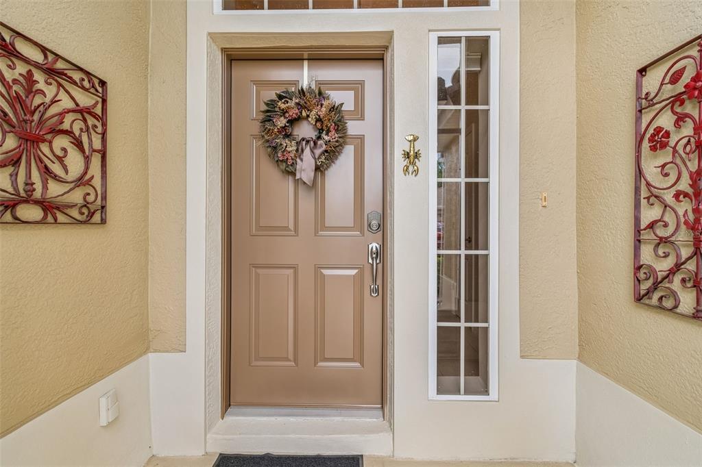 A tan front door with a wreath, sidelight window, and decorative metal wall art — 2006 GRANTHAM GREENS DRIVE UNIT 0, SUN CITY CENTER, FL
