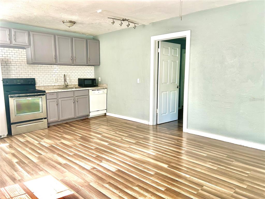 A kitchen with gray cabinets, stainless steel appliances, and wood-look flooring opens to a room — 731 FLORENCE STREET, DAYTONA BEACH, FL