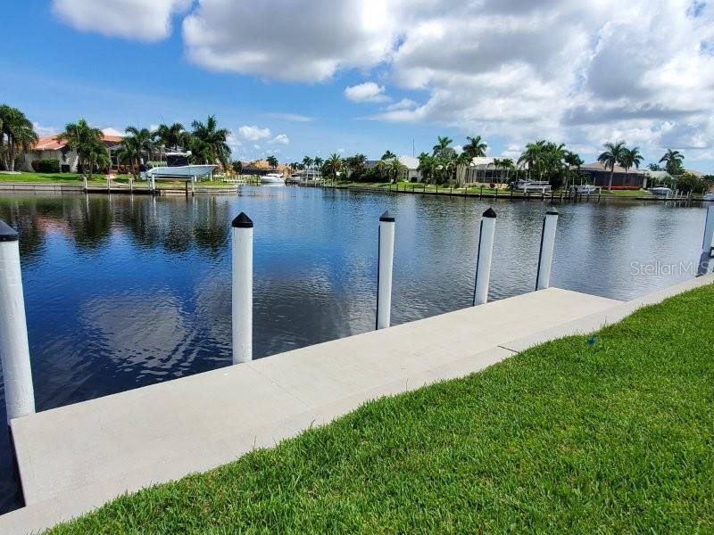A concrete dock with white pilings overlooks a canal lined with houses and palm trees — 3768 BAL HARBOR BOULEVARD UNIT 4, PUNTA GORDA, FL
