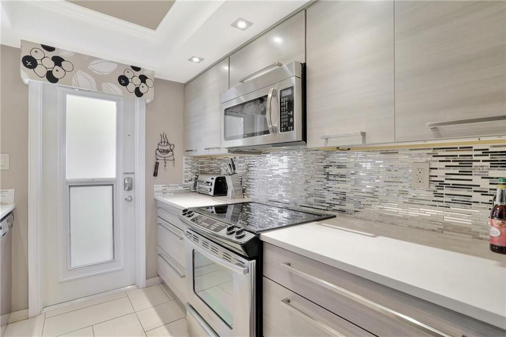 A modern kitchen features light wood cabinets, stainless steel appliances, and a mosaic tile backsplash — 505 N Riverside Drive # 4, Pompano Beach FL 33062, POMPANO BEACH, FL
