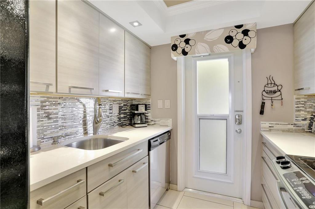 A modern kitchen features light wood cabinets, a stainless steel sink, and a glass-paneled door — 505 N Riverside Drive # 4, Pompano Beach FL 33062, POMPANO BEACH, FL