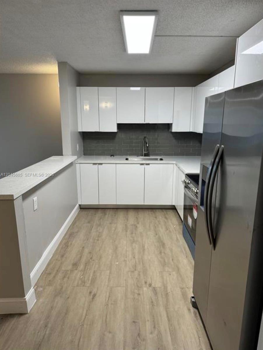 A kitchen features white cabinets, stainless steel appliances, gray tile backsplash, and light wood flooring — HOMESTEAD, FL