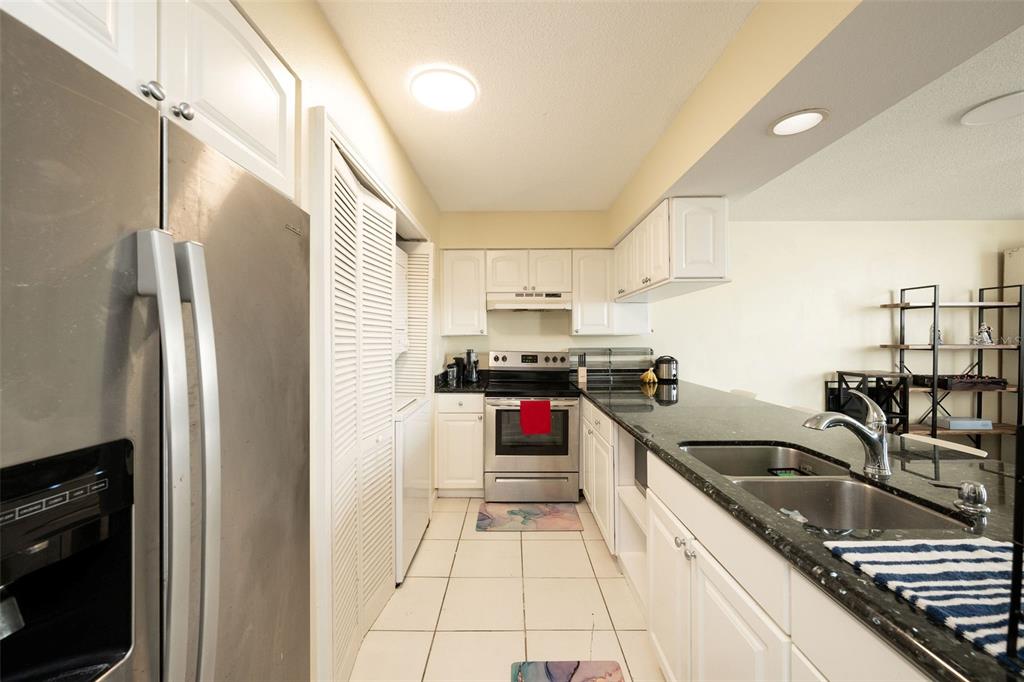 A kitchen features white cabinets, stainless steel appliances, dark countertops, and white tile flooring — 3930 S ROOSEVELT BOULEVARD UNIT S303, KEY WEST, FL