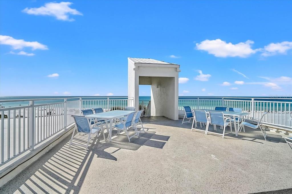 An outdoor rooftop patio features two dining tables with chairs overlooking the ocean — 6518 MIDNIGHT PASS ROAD UNIT 309, SIESTA KEY, FL