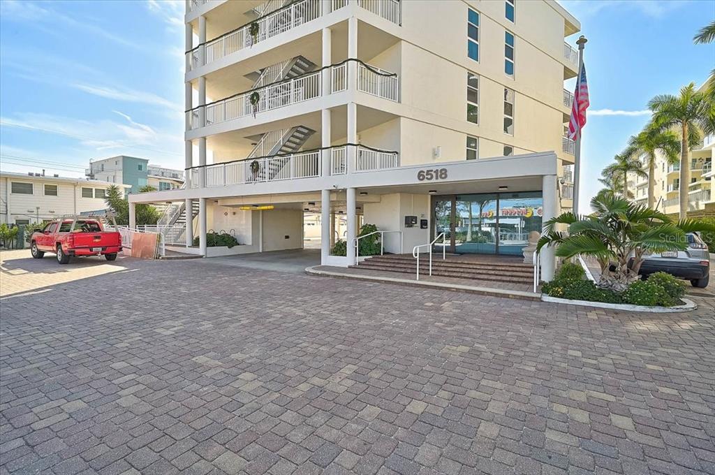 The exterior of a multi-story apartment building features a paved parking area and entrance — 6518 MIDNIGHT PASS ROAD UNIT 309, SIESTA KEY, FL