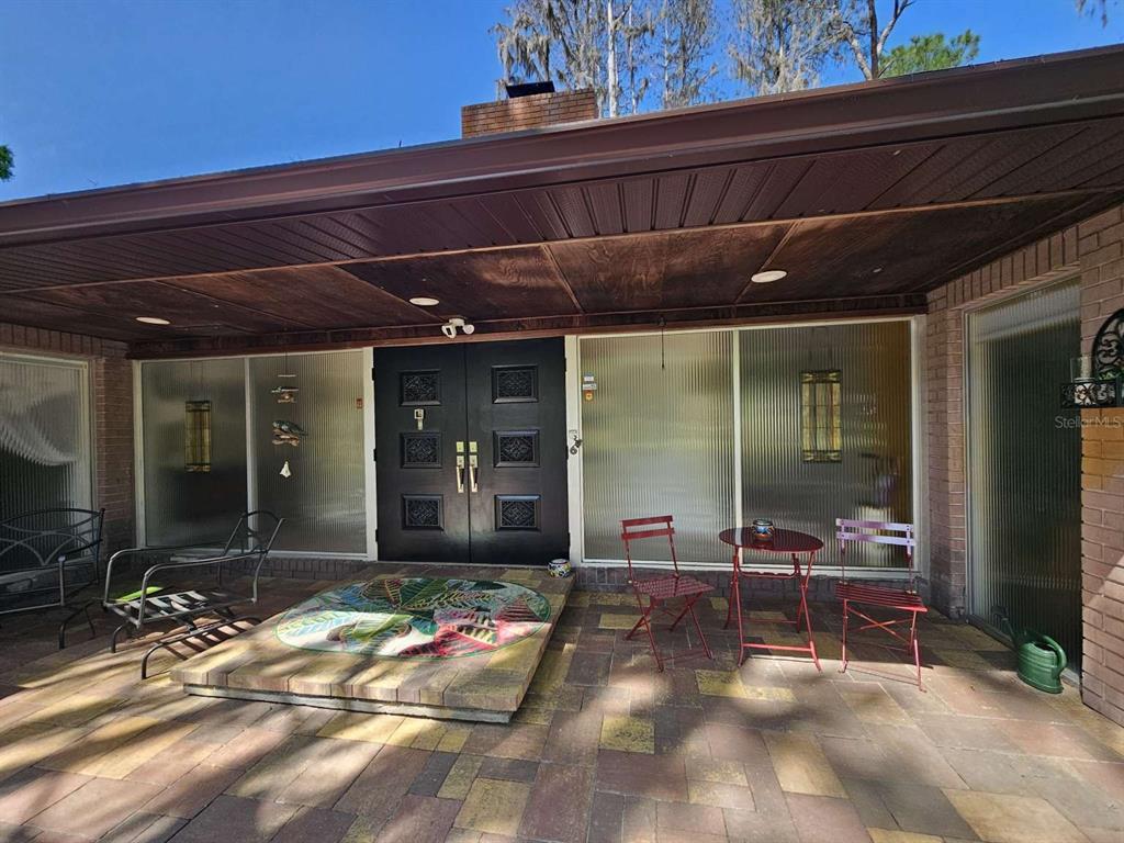 A covered brick patio features a double front door, large ribbed glass windows, and furniture — 5757 SWEET CHERRY LANE, LAND O LAKES, FL