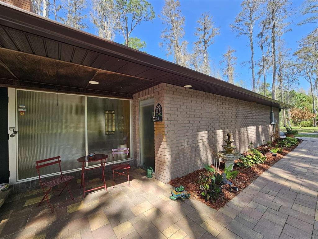 A brick-walled patio features outdoor furniture, a tiled floor, and a view of wooded grounds — 5757 SWEET CHERRY LANE, LAND O LAKES, FL