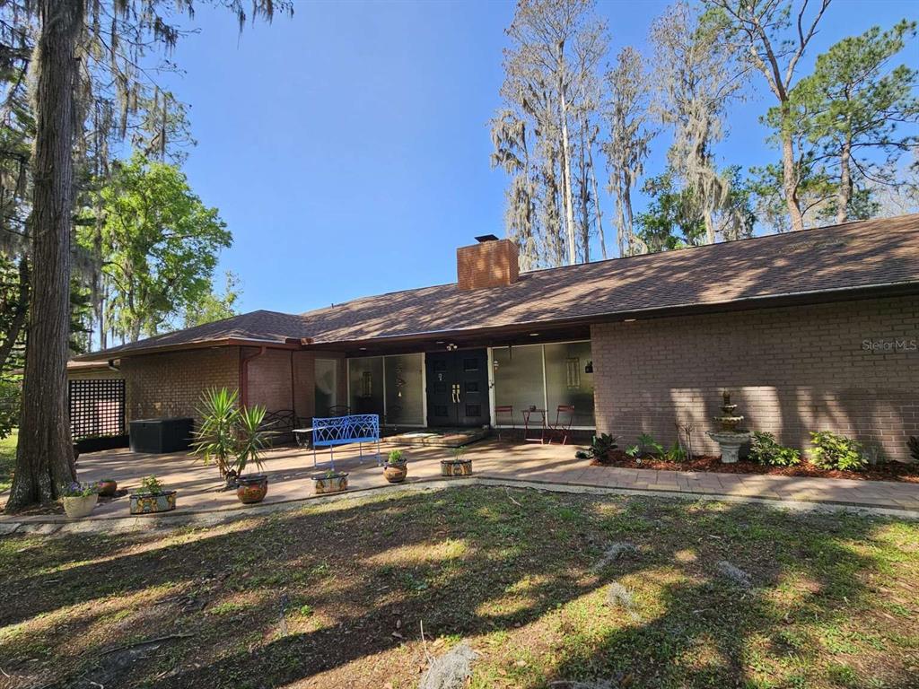 A blue metal bench sits on a paved patio overlooking a wooded backyard — 5757 SWEET CHERRY LANE, LAND O LAKES, FL