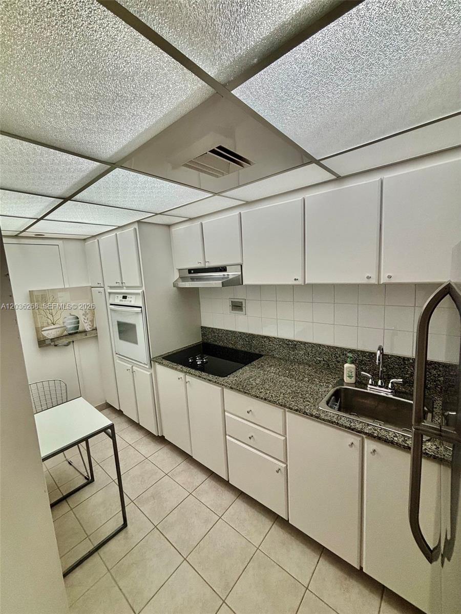 This galley kitchen features white cabinets, granite countertops, and a drop ceiling with lights — 1000 West Ave # 822, Miami Beach FL 33139, MIAMI BEACH, FL